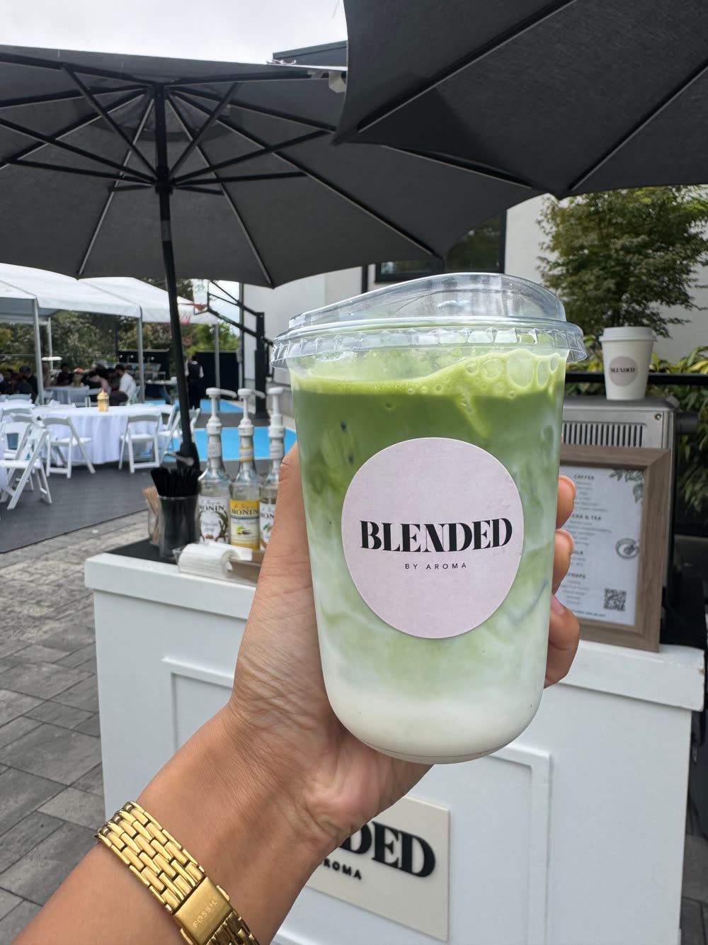 Iced matcha latte with a Blended by Aroma sticker at an outdoor event
